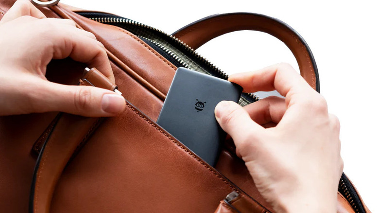 Image of a Pebblebee card-shaped wallet tracker being placed into the pocket of a brown leather purse. Two hands are visible in the image.