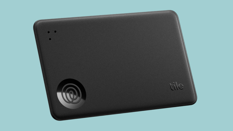 Photo of the Tile Slim card-shaped wallet tracker. A black credit card-sized device with the Life360 logo and the embossed word "tile"