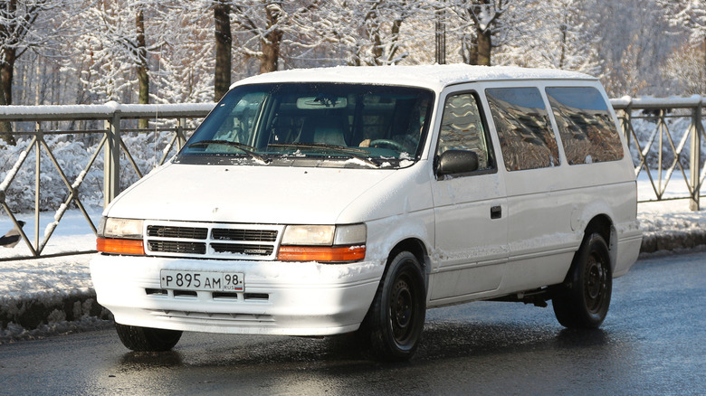 A white 1990s Dodge Caravan driven on snowy road.