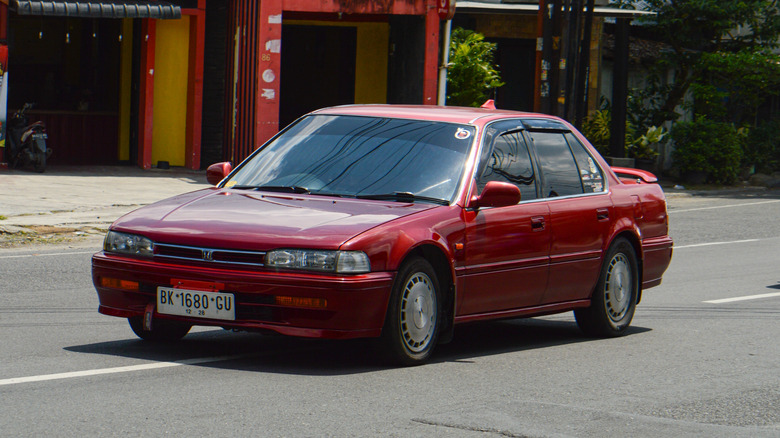 A red 1993 Honda Accord sedan being driven down an urban road.