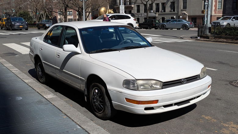 A white 1994 Toyota Camry parked roadside in a city.