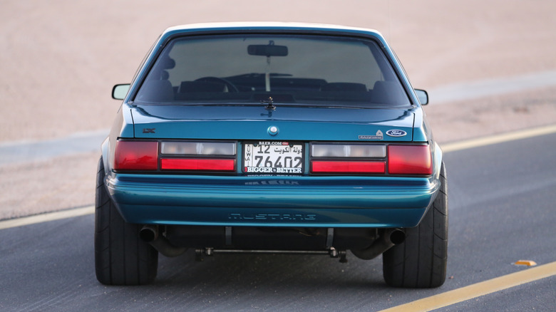 A rear-end view of a parked wide-track blue Ford Mustang Fox Body from the 1980s.