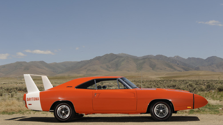 An orange 1969 Dodge Charger Daytona Nascar race car standing on a dirt surface complete with nose cone and white wing.