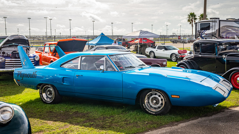 A blue Plymouth Road Runner Superbird with its nose cone and wing at an outdoor car show on grass.