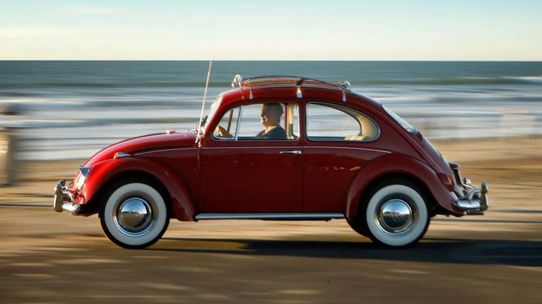 a restored red Volkswagen Beetle being driven near the beach