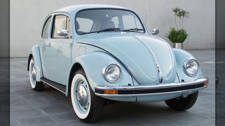 a blue 2003 Volkswagen Beetle parked in the enclosed courtyard of building with green plants in the background