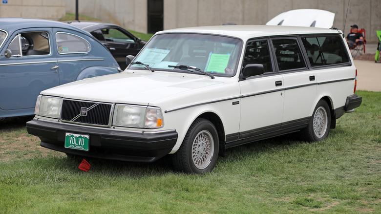 White Volvo 240 wagon parked in grass, front-left 3/4 view