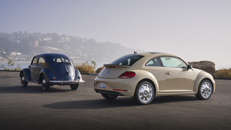 Black 1949 Beetle and tan 2019 Beetle Final Edition parked on an overlook together, both seen at an angle from behind