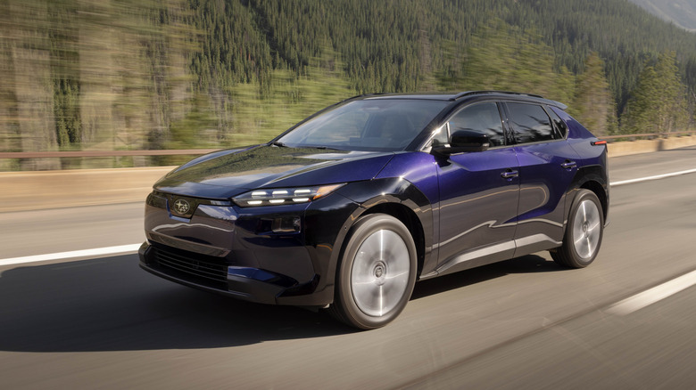 Front 3/4 view of dark blue Subaru Solterra EV on forest highway.