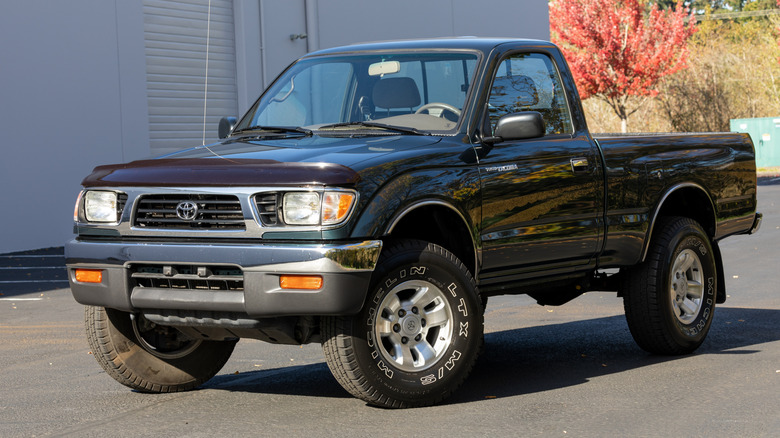 An old, dark green Toyota Tacoma with a regular cab parked next to a building.