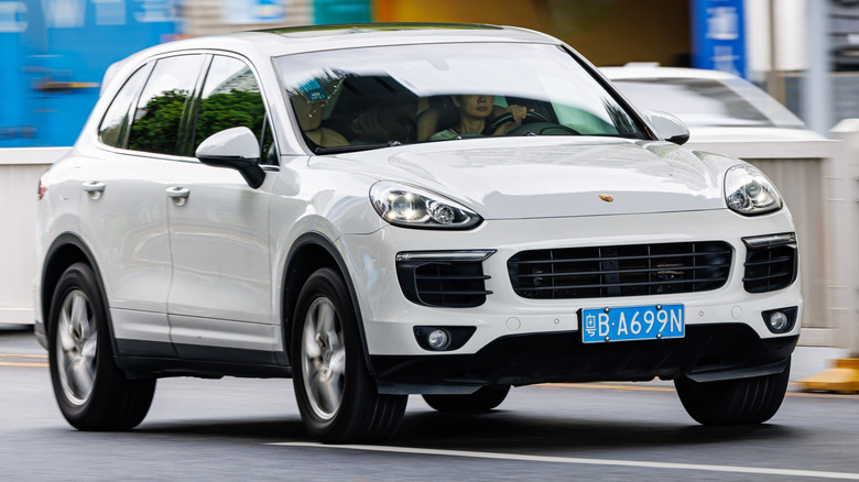 2013 Porsche Cayenne in white driving down a busy road, front 3/4 view, China license plates