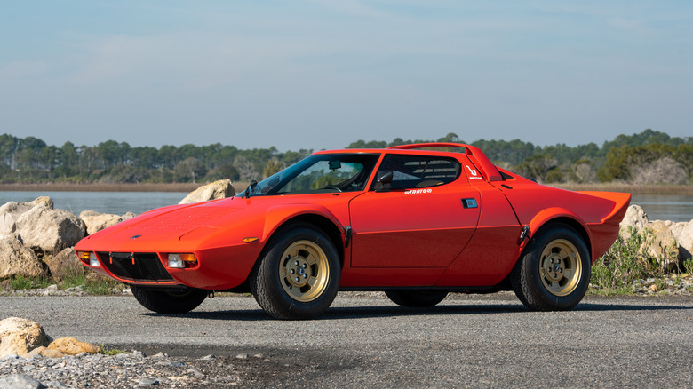 Red Lancia Stratos HF parked in front of rocks with water in the distance