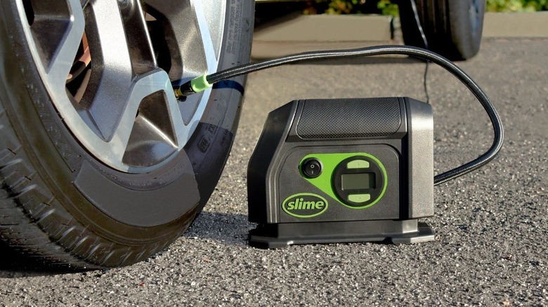 A portable air compressor branded Slime filling a car tire
