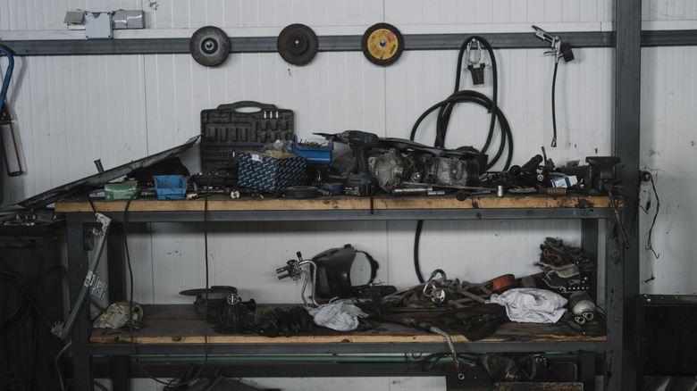 A workbench in a garage holds various tools and machine parts. Some items are organized while others are messy.