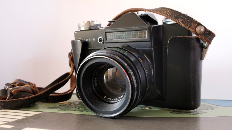 a black Zenit-E camera with a case and strap on a desk