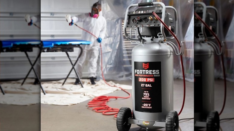 Fortress 27 Gallon 200 PSI Oil-Free Vertical Shop/Auto Air Compressor in foreground while user paints in background