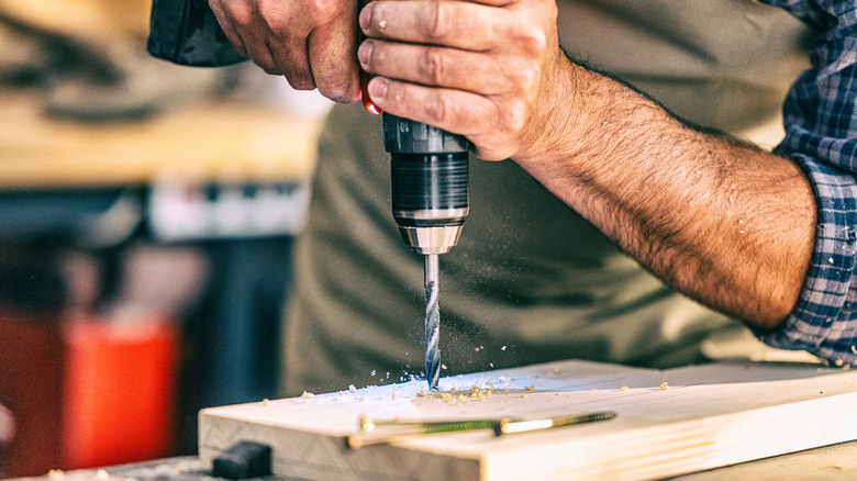 A man drills a hole with a drill on a piece of wood .