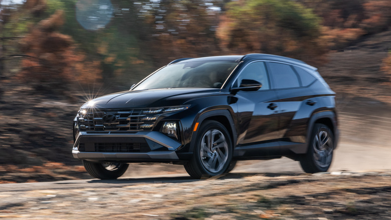 Black 2026 Hyundai Tucson Hybrid driving on forest trail.