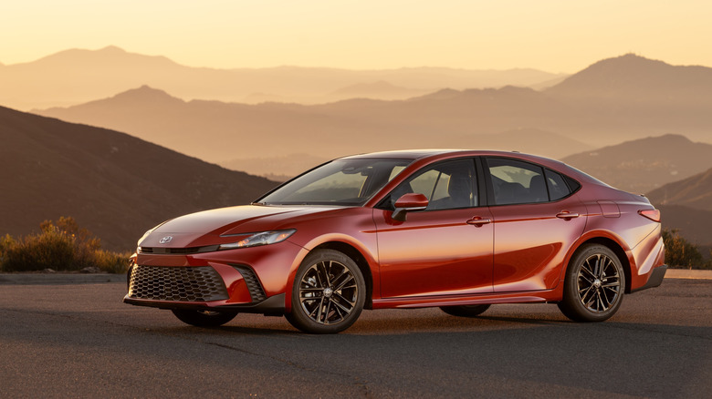 Red 2026 Toyota Camry SE parked at sunset in front of mountains.