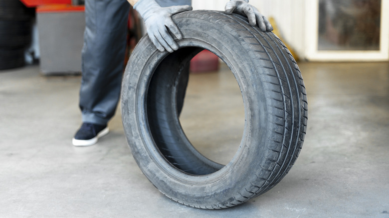 A mechanic wearing gloves rolls a tire inside a workshop.
