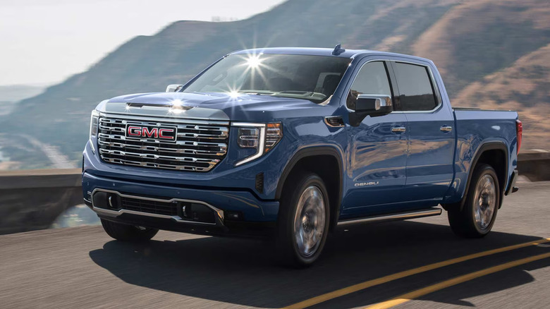 blue GMC Sierra 1500 Denali reflecting sunlight on mountain road