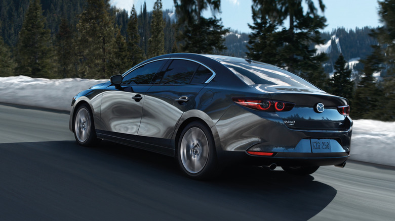 Gray current-generation Mazda 3 sedan seen from left rear on a snowy mountain road