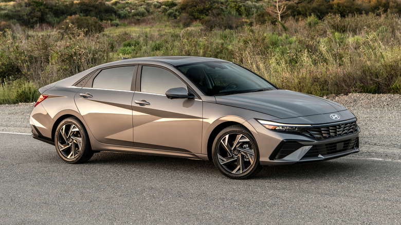 Front 3/4 view of a gray 2026 Hyundai Elantra parked in front of long grass