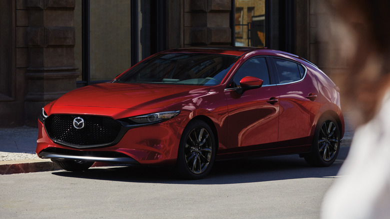 Passerby stares at a red 2026 Mazda3 parked on a city street