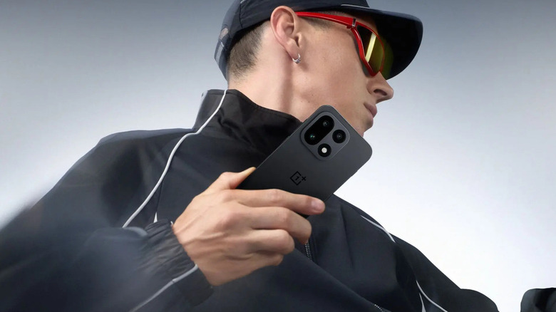 A person dressed in black poses with the OnePlus 15.