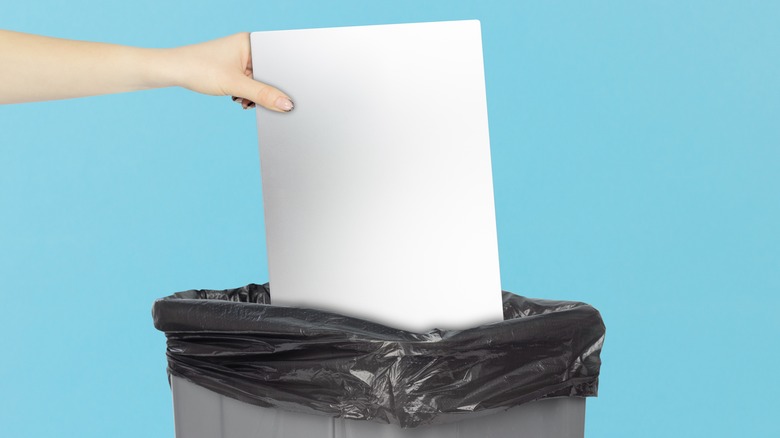 A hand throwing a laptop in the trash, blue background