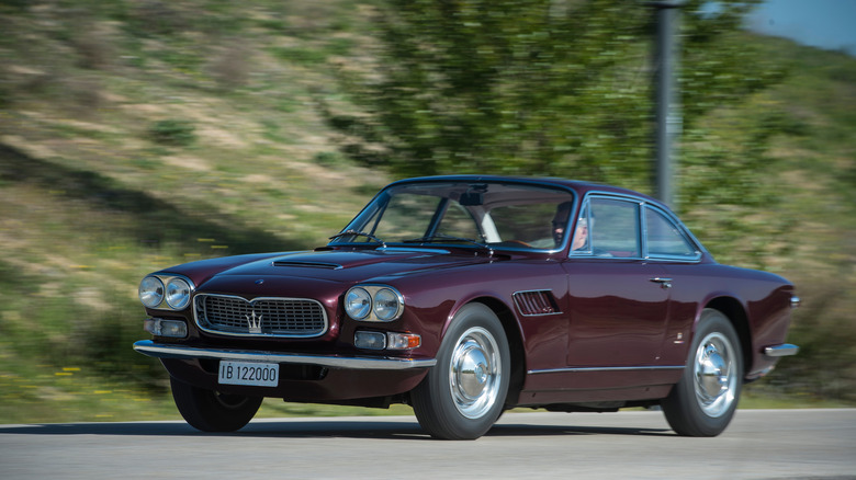 A burgundy Maserati 3500 Series One Sebring driving down a forested country road.