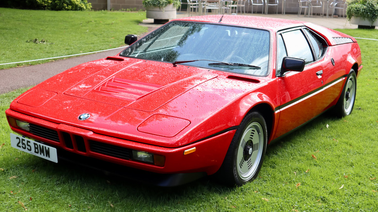 A red 1980s BMW M1 parked on a grass field.