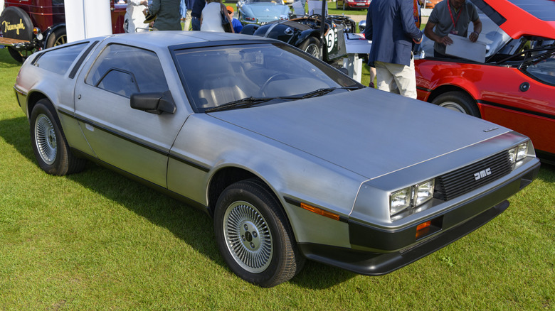 A silver DeLorean DMC-12 parked on a grass field.