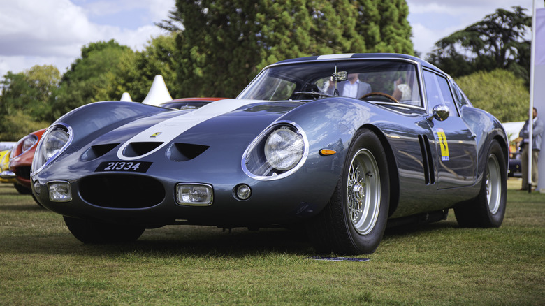 A light blue 1960s Ferrari 250 GTO parked on a grass field.