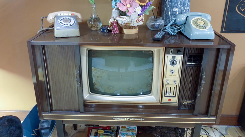 Wooden console TV set with home knickknacks and rotary phones placed atop it.