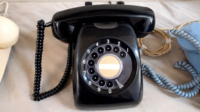 A black rotary phone resting next to other rotary phones.