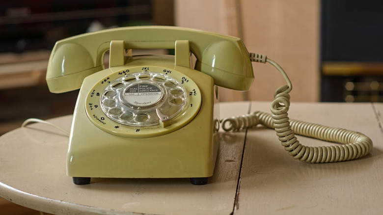 Close-up of a pale green rotary phone sitting on a white wood table