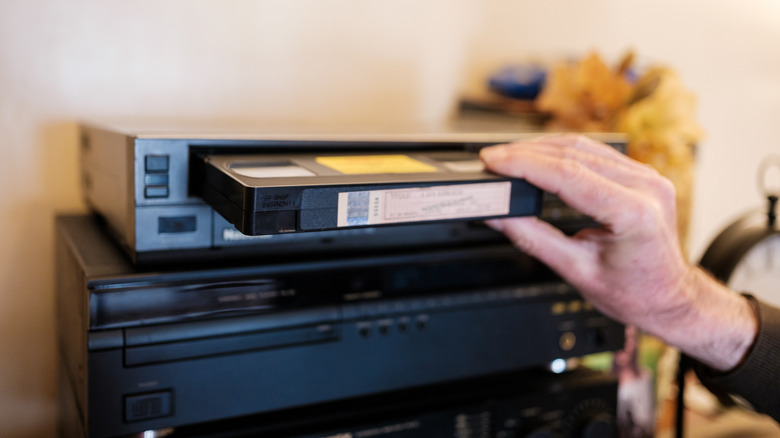 A hand inserting a VHS tape into a black VCR