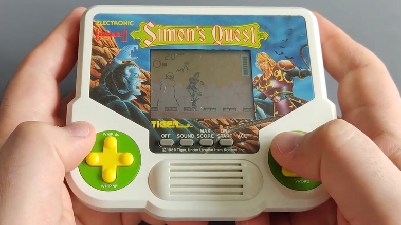 Two hands holding and playing the Tiger Electronics Castlevania II: Simon's Quest game on a grey background