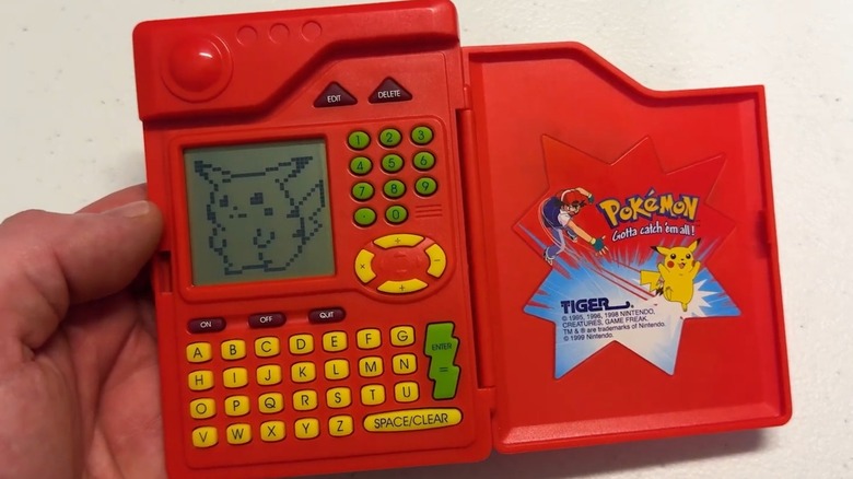 A hand holding the Tiger Electronics Pokémon Pokédex flipped open with Pikachu on the screen