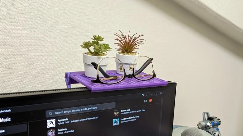 A purple mini monitor shelf on a screen holding plants and glasses.