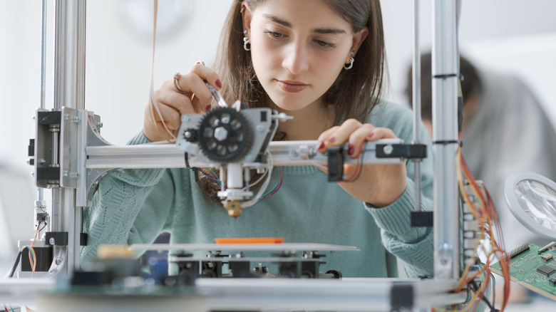 Someone using a 3D printer with orange filament.