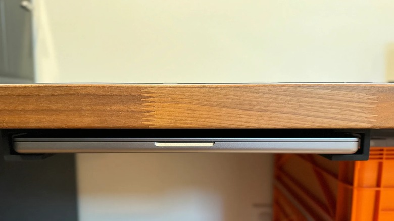 A narrow shelf tucked under a desk holding a laptop.