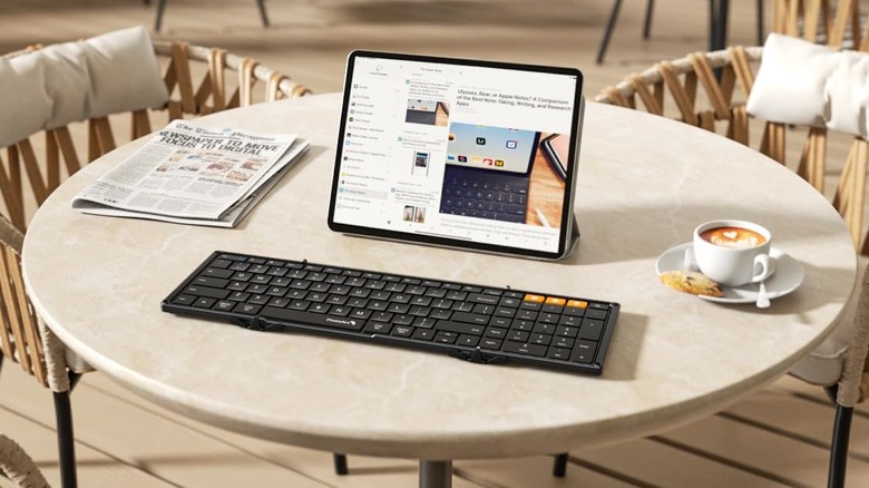 A foldable keyboard on a café table, newspaper, iPad and coffee cup next to it