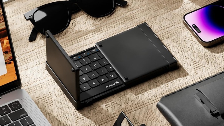 Foldable keyboard with laptop, sunglasses, and phone next to it