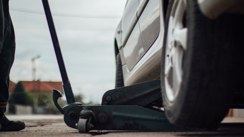 A tire technician lifting a car with a car jack .