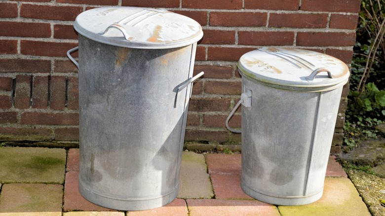 Two trashcans side by side near a brick wall.