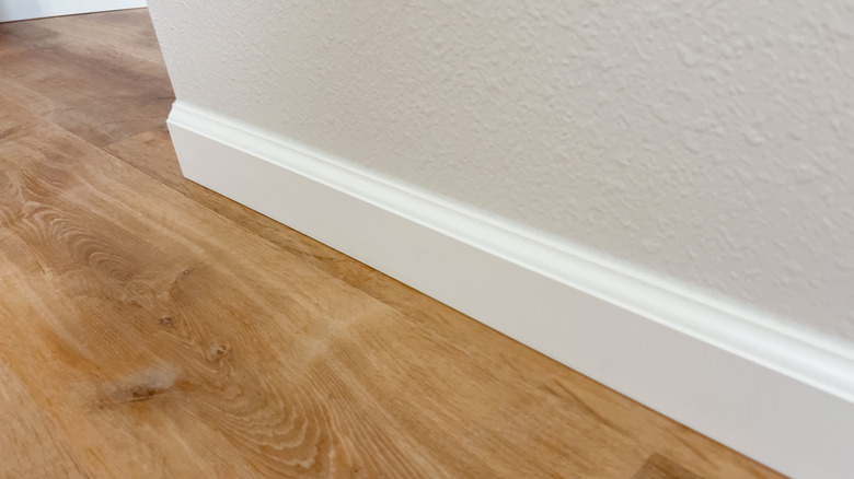 A baseboard running alongside a white wall, meeting the wooden flooring