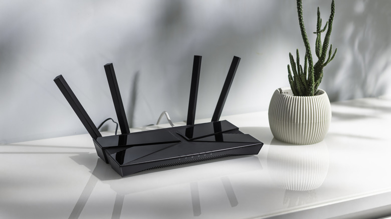 A black router on a table next to a cactus plant, with its wires behind the furniture