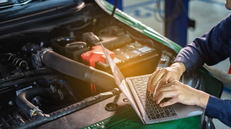 an auto mechanic using a laptop to conduct engine diagnostics